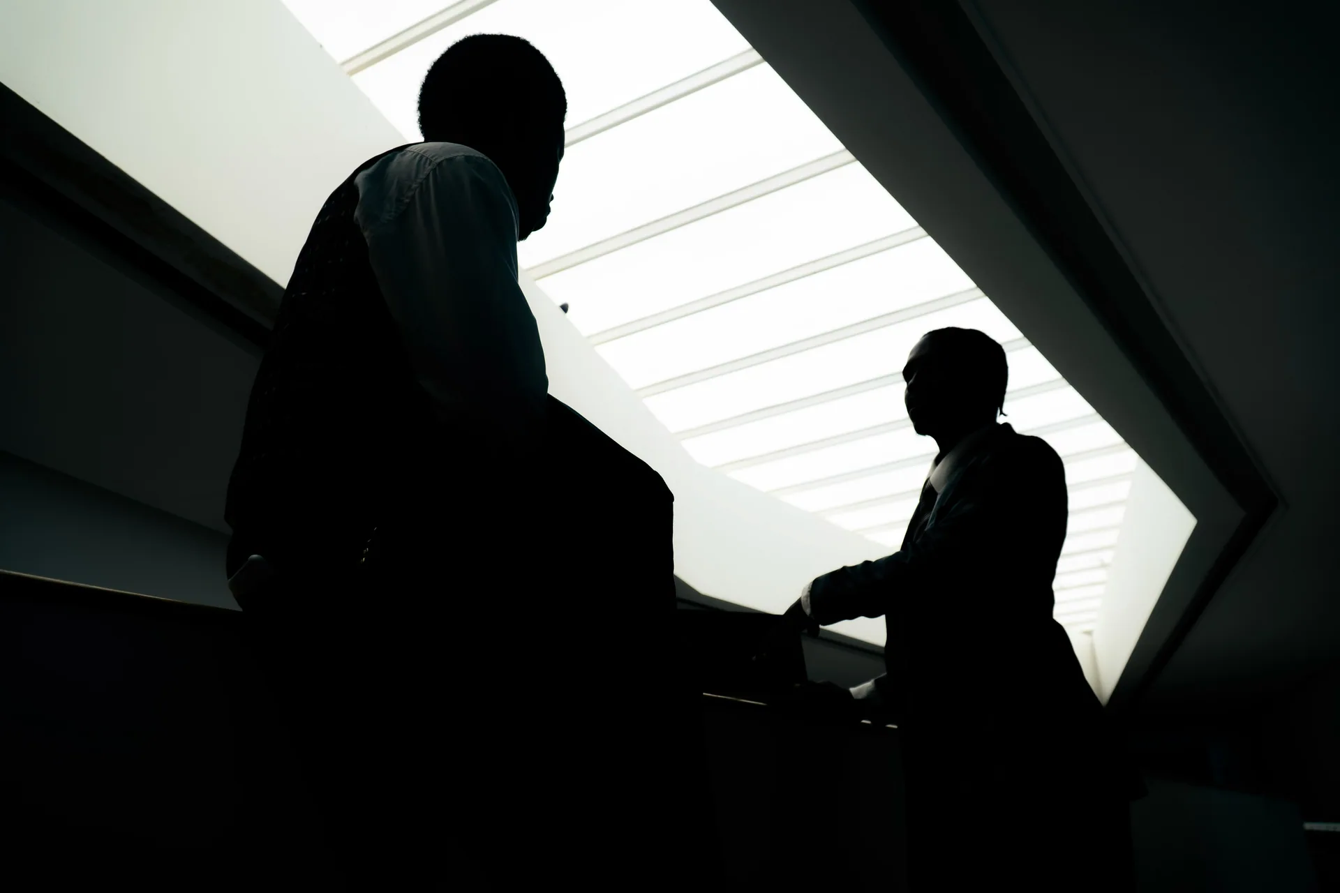 Silhouettes of businesspeople talking beneath a bright skylight